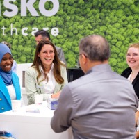 Gesprächssituation am Messestand: Sechs Personen lachen sich an. Gesprächssituation am Messestand: Sechs Personen lachen sich an.