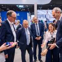 Messebesucher im Anzug betrachten eine moderne Armprothese, die von Ausstellern präsentiert wird. Messebesucher im Anzug betrachten eine moderne Armprothese, die von Ausstellern präsentiert wird.