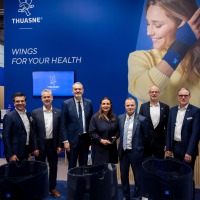 Gruppenfoto von Messebesuchern am Stand von Thuasne auf der OTWorld, vor einer blauen Wand mit dem Slogan ‚Wings for your health‘ und einem großen Bild einer Frau mit Handbandage Gruppenfoto von Messebesuchern am Stand von Thuasne auf der OTWorld, vor einer blauen Wand mit dem Slogan ‚Wings for your health‘ und einem großen Bild einer Frau mit Handbandage