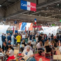 Viele Menschen an Tischen, redend, essend und trinkend. Über der Szene ein Banner mit der Aufschrift Café de Paris. Viele Menschen an Tischen, redend, essend und trinkend. Über der Szene ein Banner mit der Aufschrift Café de Paris.