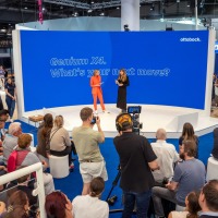 Eine Bühne mit zwei Sprecherinnen vor einer blauen Rückwand, davor zahlreiche Zuhörer und ein Kameramann.  Eine Bühne mit zwei Sprecherinnen vor einer blauen Rückwand, davor zahlreiche Zuhörer und ein Kameramann.