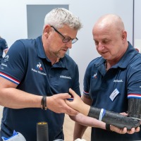 Exhibitor demonstrates a modern hand prosthesis at OT-World while several visitors listen attentively and examine other prosthetic models. Exhibitor demonstrates a modern hand prosthesis at OT-World while several visitors listen attentively and examine other prosthetic models.