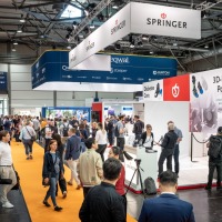 Volle Messehalle auf der OTWorld mit Besucherinnen und Besuchern entlang eines orangefarbenen Teppichwegs, vorbei an Messeständen Volle Messehalle auf der OTWorld mit Besucherinnen und Besuchern entlang eines orangefarbenen Teppichwegs, vorbei an Messeständen