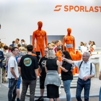 Am Stand von SPORLASTIC herrscht reges Treiben – Besucher und Fachleute tauschen sich aus und begutachten orangefarbene Demonstrationsmodelle für orthopädische Anwendungen. Am Stand von SPORLASTIC herrscht reges Treiben – Besucher und Fachleute tauschen sich aus und begutachten orangefarbene Demonstrationsmodelle für orthopädische Anwendungen.